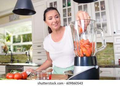 Attractive woman making smoothie in blender in modern kitchen - Powered by Shutterstock