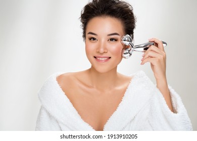 Attractive woman massaging her cheek with massage Y-shaped ball roller on light blue background. Beauty and Skin care concept. Plus size model - Powered by Shutterstock