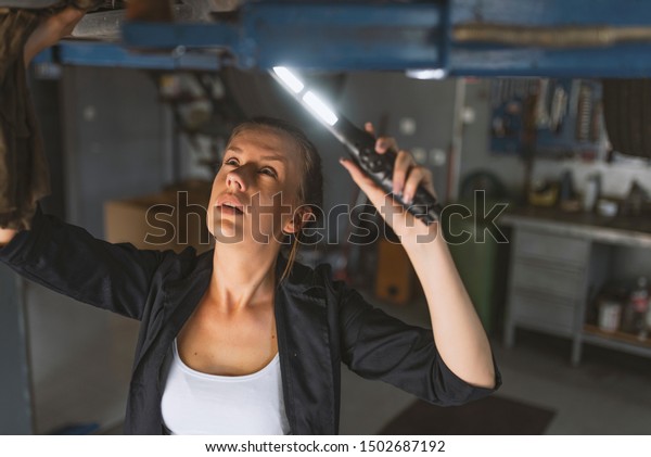 An attractive woman mechanic working on a car in\
a repair shop. Portrait Of Female Auto Mechanic Working Underneath\
Car. Making some adjustments to her car. Proud female garage\
mechanic