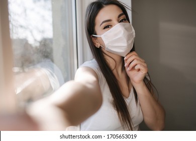 Attractive woman in medical mask make selfie at home. Female in white t'shirt and white medical mask use phone - Powered by Shutterstock