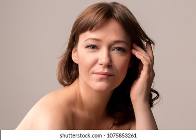 Attractive woman with natural makeup gently touching her hair. Posing on camera. Beauty concept. Mid age woman over 35 years old concept.