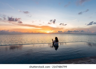 Attractive woman on a infinity pool near the ocean with a glass of champagne.Back view - Powered by Shutterstock