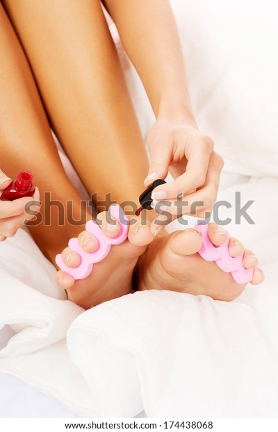 Attractive woman painting\
her toes in bed.