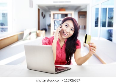 An Attractive Woman Purchasing Product Online Using Her Laptop Computer, Credit Card, And Mobile Phone, Shot At Home