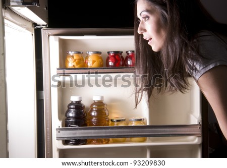 An attractive woman raids the refrigerator late at night looking for a food snack