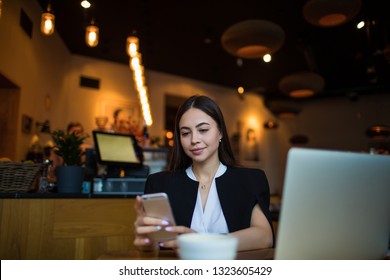 Attractive woman real estate analyst reading e-mail on mobil phone while sitting in restaurant during coffee break. Female leadership browsing wifi on smartphone gadget, resting in cafe during leisure - Shutterstock ID 1323605429