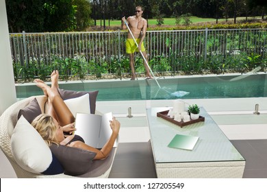 Attractive Woman Relaxing In Backyard Patio With Pool Boy Cleaning The Pool