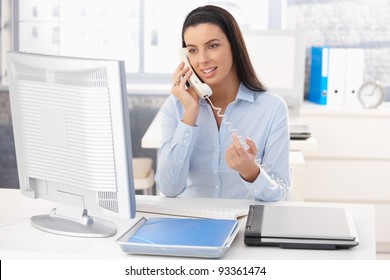 Attractive Woman Sitting At Desk At Work On Landline Phone Call, Gesturing, Smiling.?