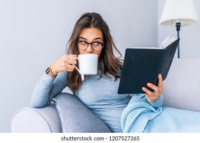 Attractive woman sitting on bed in the morning, drinking tea, reading book, curly hair, casual style, blue jeans, white sweater, feeling comfortable at home, having rest, smiling - Shutterstock ID 1207527265