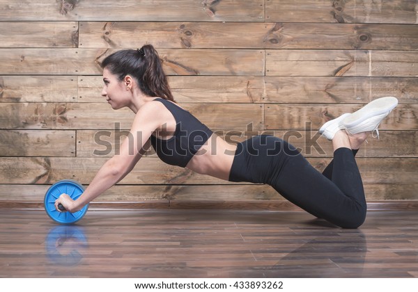 Attractive woman with\
slim stomach do abdominal exercises with wheel. Workout exercise at\
home to lose weight