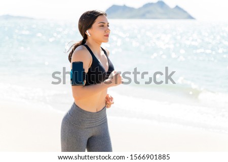 Attractive woman with smartphone jogging at beach during summer