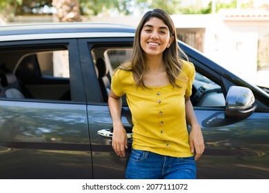 Attractive woman smiling and making eye contact while standing next to the black car outside her house