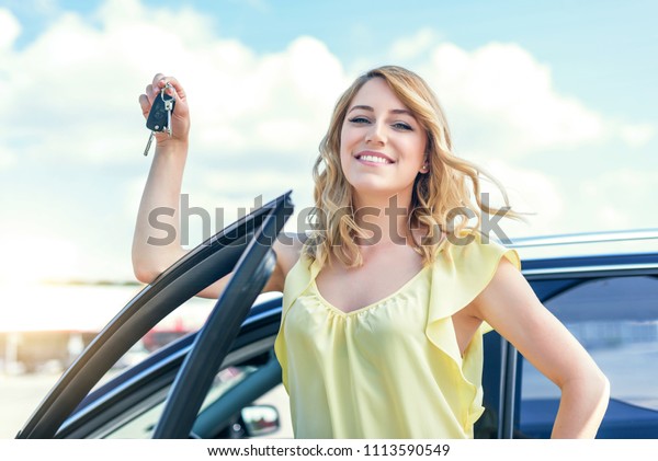 An attractive woman\
standing near the car holds a car key in her hand. Rent or purchase\
of auto - concept.