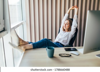 Attractive Woman Stretching Body And Relaxing At The Office With Legs Up On A Desk.