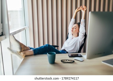 Attractive Woman Stretching Body And Relaxing At The Office With Legs Up On A Desk.