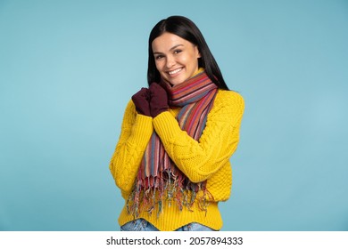 Attractive woman in stylish yellow sweater smiles widely. Cool girl in warm knitted scarf and gloves posing on blue background. Winter concept 