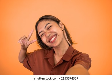 attractive woman take a selfie using mobile phone camera with v sign finger gesture on isolated background