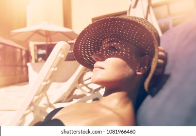 Attractive Woman Tanning On The Beach, Lying Down On Sunbed And Taking Sun, Nice Female Hides Her Face From The Sun Under A Straw Hat, Summer Vacation Concept                               