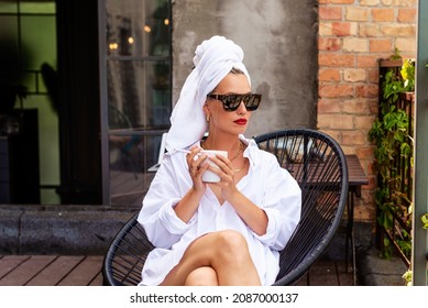 Attractive woman with towel turban on head wearing sunglasses while having having coffee on balcony and smoking cigarette in the morning. - Powered by Shutterstock