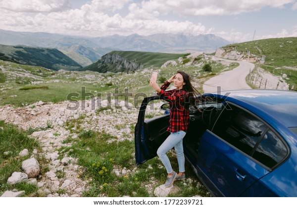 attractive woman travel by\
car and using smartphone in mountains. Holiday maker female on road\
trip by car to mountains countryside taking photo on smartphone\
camera.