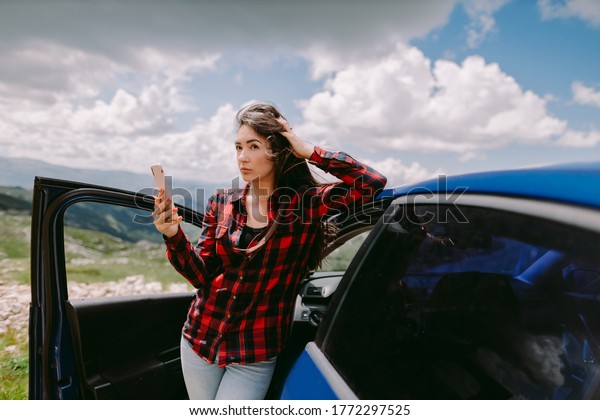 attractive woman\
travel by car and using smartphone in mountains. Beautiful female\
tourist on road trip by car to mountains browsing phone. Vacations\
summer time on\
lockdown.