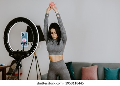 Attractive Woman Virtual Workout At Home Using Smartphone. Fitness Workout Exercises Online Woman At Home. Fitness Influencer Personal Trainer Coach Recording On Smartphone Camera New Content For