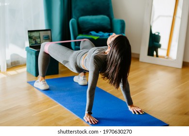 Attractive Woman Virtual Workout At Home Using Laptop. Fitness Workout Exercises Online Woman At Home. . Virtual Online Fitness Course At Home. Elastic Band Glutes Workout.