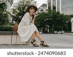 attractive woman walking in street on vacation dressed in white summer fashion dress straw hat sunglasses and purse, smiling happy having fun, stylish accessories trend