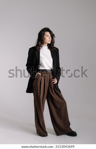 Attractive woman wear business look.\
Brunette model wear white shirt, black men\'s jacket and brown baggy\
pants. Winter, fall autumn or spring minimal\
outfit.