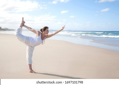 Attractive Woman Wearing All White, Doing A Lord Of The Dance (Natarajasana) Yoga Pose On The Beach.