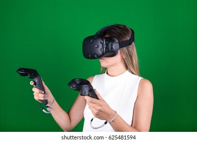 attractive woman wearing virtual reality headset with two handheld trackpads or controllers in green screen studio - Powered by Shutterstock