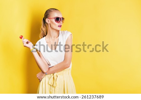 attractive woman in white top with lollipop in hand on yellow background
