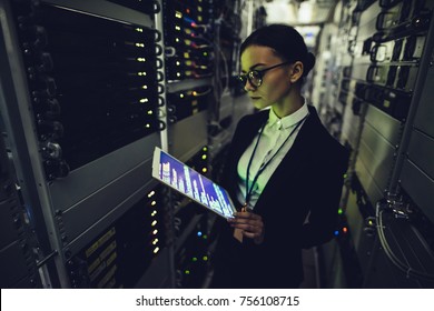 Attractive woman is working in data centre with tablet.IT engineer specialist in network server room.Running diagnostics and maintenance.Technician examining server in data center full of rack servers