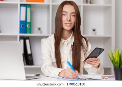 Attractive woman working on smart phone in her workstation.