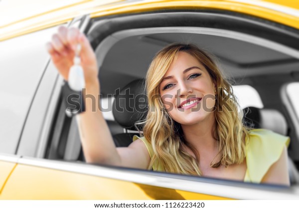 An attractive woman\
in the yellow car holds a car key in her hand. Rent or purchase of\
auto - concept.