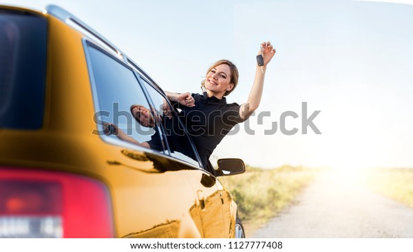 An attractive woman\
in the yellow car holds a car key in her hand. Rent or purchase of\
auto - concept.