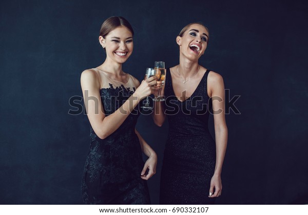Attractive women in cocktail dresses are\
holding glasses of champagne, talking and\
smiling.