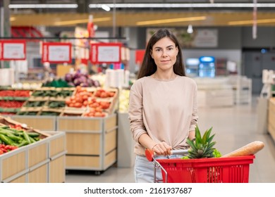 Attractive Young Adult Woman Wearing Casual Clothes Standing With Shopping Cart In Store Aisle