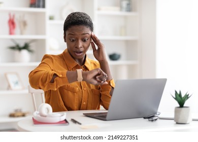 Attractive young african american business woman sitting at workdesk in front of laptop, working online, looking at watch and touching head, got late for business meeting, office interior, copy space - Shutterstock ID 2149227351