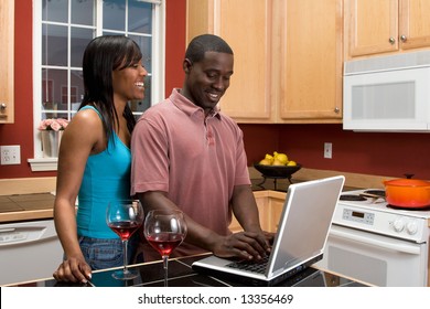 Attractive Young African American Couple Laughing Together In Their Kitchen While Looking At Something On A Computer Screen.