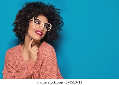 Attractive young African American girl with afro hairstyle and glamour makeup posing in fashionable sweater on blue background.
