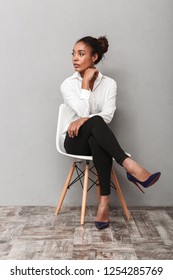 Attractive Young African Business Woman Wearing Shirt Sitting In A Chair Isolated Over Gray Background, Looking Away At Copy Space