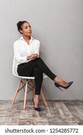 Attractive Young African Business Woman Wearing Shirt Sitting In A Chair Isolated Over Gray Background, Looking Away At Copy Space