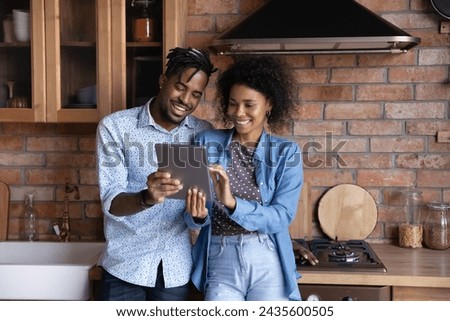 Attractive young African couple holding digital tablet choose interior design on internet for further remodelling of kitchen, make food order through supermarket virtual app, modern tech usage concept