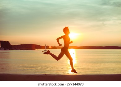 Attractive young African girl athlete running at sunset or sunrise along the beach