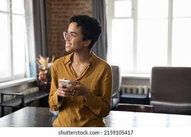 Attractive young African woman standing in office staring into distance while holds cell phone in hands. Enjoy new app usage, share messages, single lady using electronic date on-line services concept - Shutterstock ID 2159105417