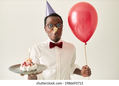 Attractive Young Afro American Male Posing Isolated With Helium Balloon And Cake With Burning Candle Blowing Party Horn Congratulating Girlfriend On Birthday, Having Overjoyed Excited Look