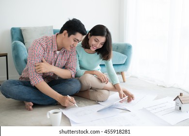 Attractive Young Asian Adult Couple Looking At House Plans.