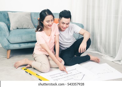 Attractive Young Asian Adult Couple Looking At House Plans.