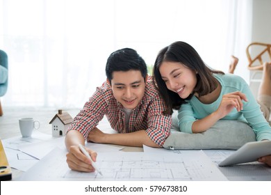 Attractive Young Asian Adult Couple Looking At House Plans.